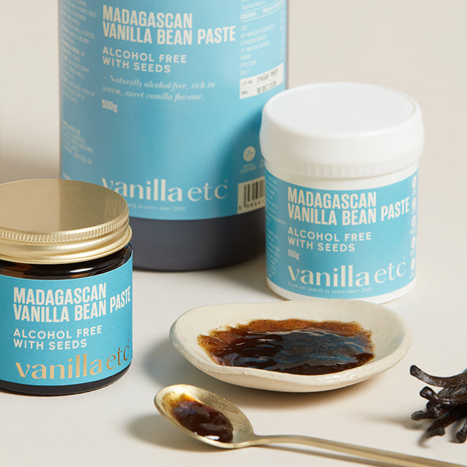 Vanilla bean paste containers with a spoonful of paste on a neutral background