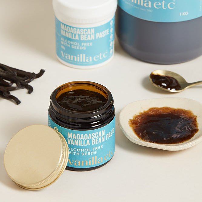 Vanilla bean paste jars and a container with vanilla beans on a white background