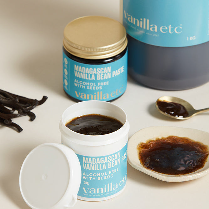 Vanilla bean paste containers with vanilla beans and a spoon on a light background