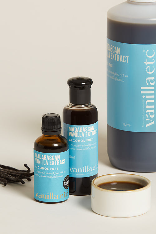 Three bottles of vanilla extract with a cup of vanilla extract on a light background
