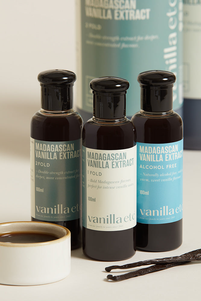 Three bottles of 100ml extract of different types, 1 fold,  2 fold and alcohol free, stood next to an earthenware bowl of extract and two whole beans.