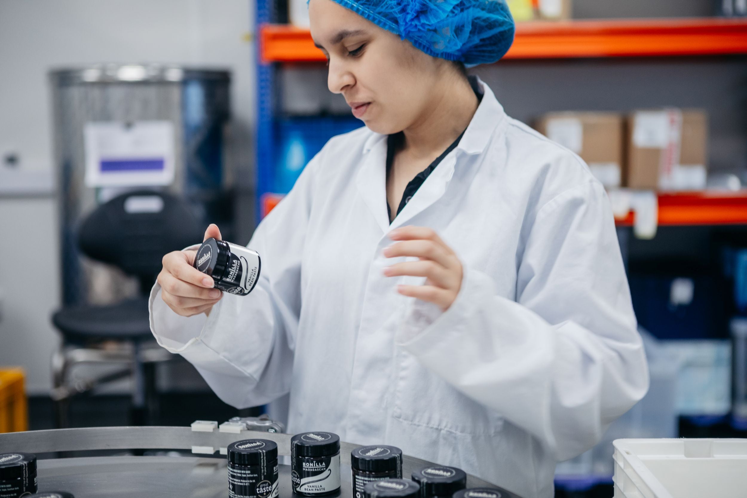 Person in a lab coat and blue hairnet working with containers in a vanilla factory setting.
