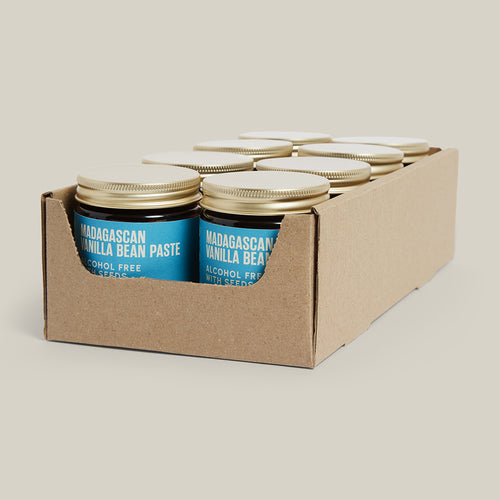 Box of Madagascan Vanilla Bean Paste jars with gold lids on a beige background