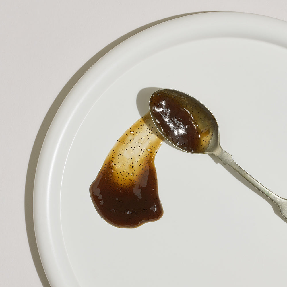 Spoon with vanilla bean paste on a white plate showing consistency and seeds