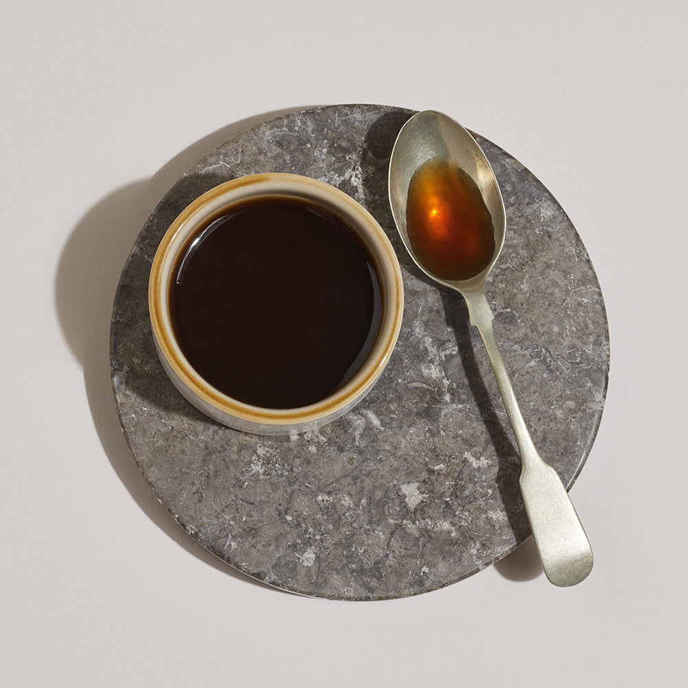 Cup of vanilla extract with a spoonful of vanilla extract on a stone coaster