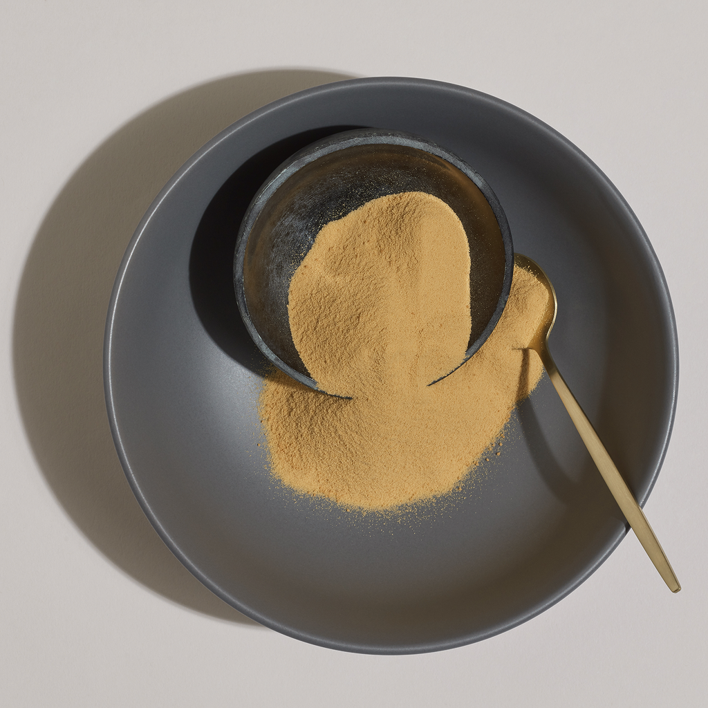 Dark bowl with gold powder and a spoon on a light gray background