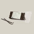Vacuum packaged Madagascar vanilla pods with label, two separate beans laid in front, all  on a cream background.