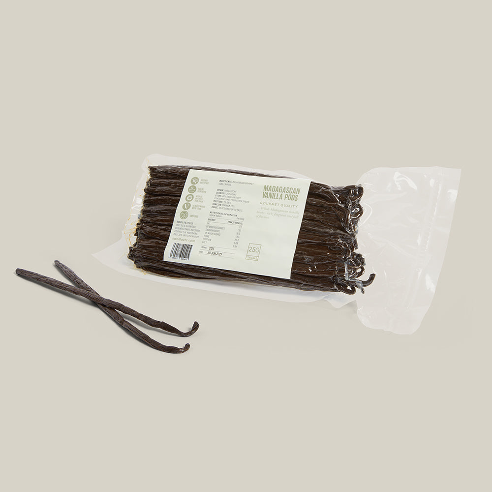 Vacuum packaged Madagascar vanilla pods with label, two separate beans laid in front, all  on a cream background.